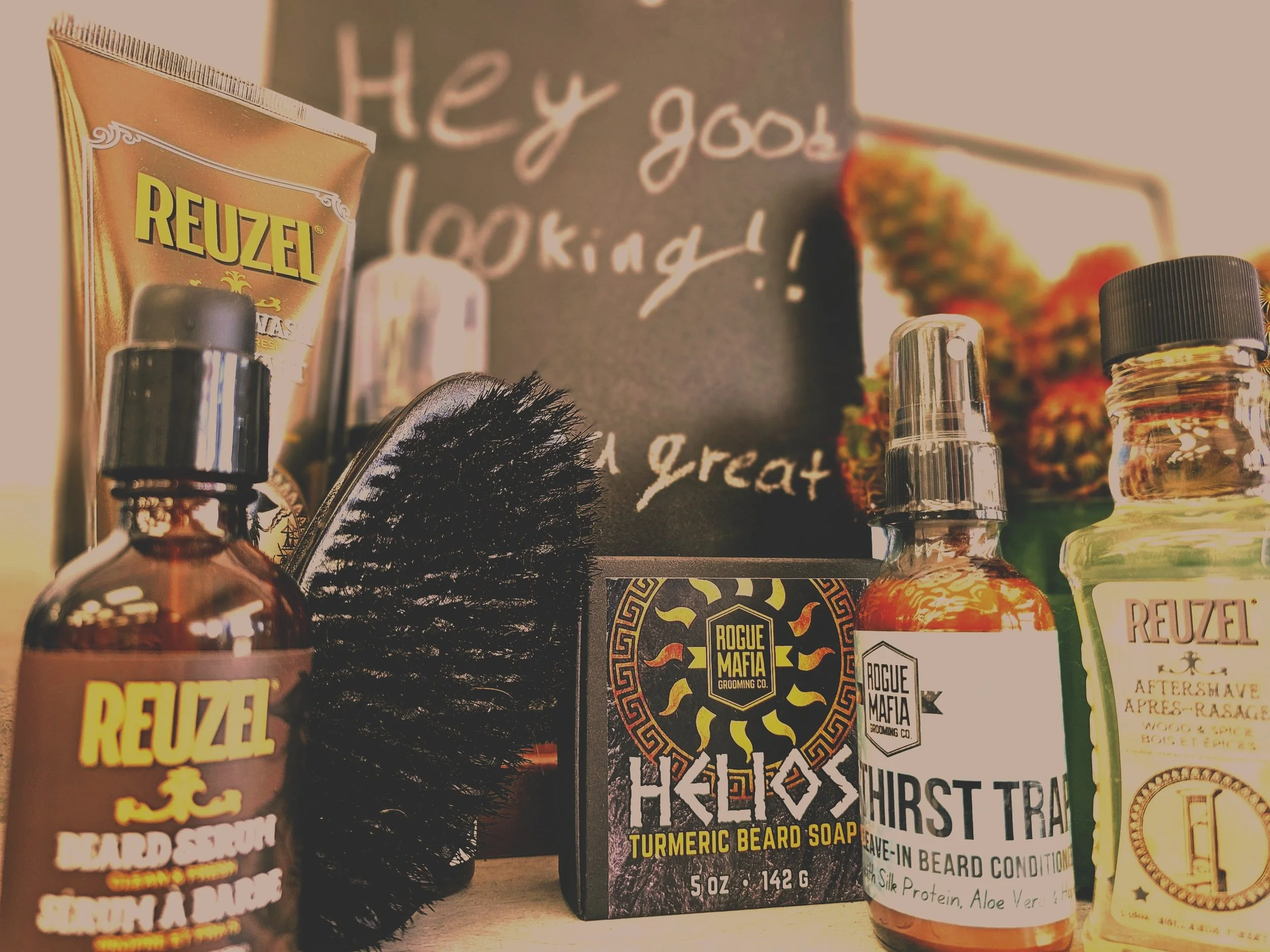 Various beard grooming products arranged in front of a chalkboard sign that reads "Hey good looking!!"