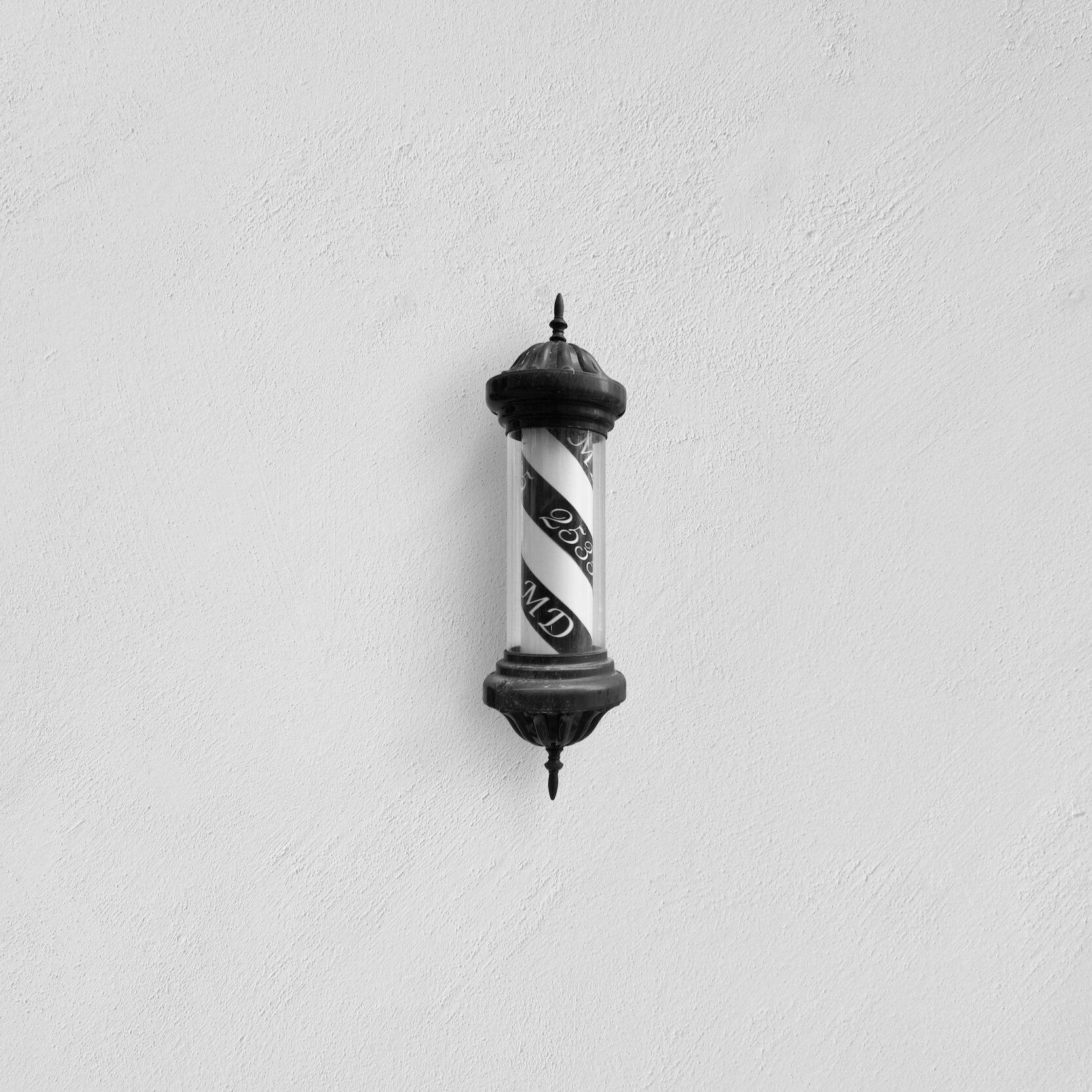 Barber pole with red and white spiral stripes on textured white wall.