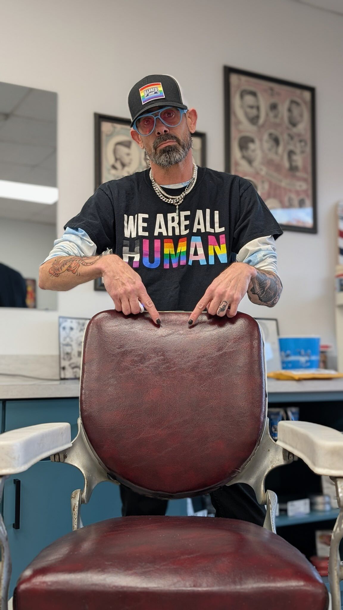 Man in a jersey giving a haircut to a small dog in a barber chair. Barbershop interior.