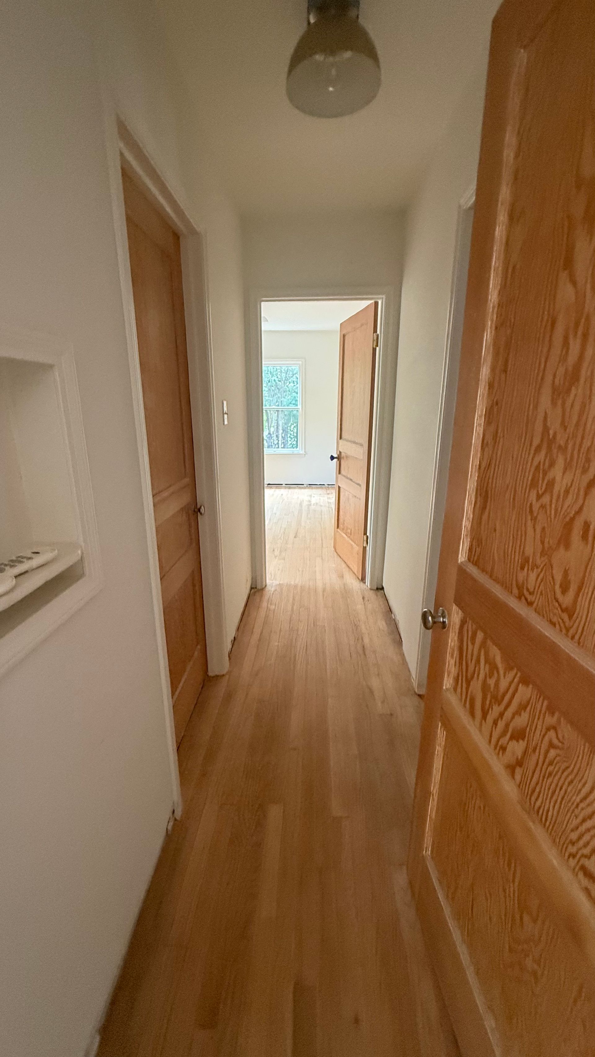Hallway with wooden floors and doors leading to rooms. Light floods into the distant room.