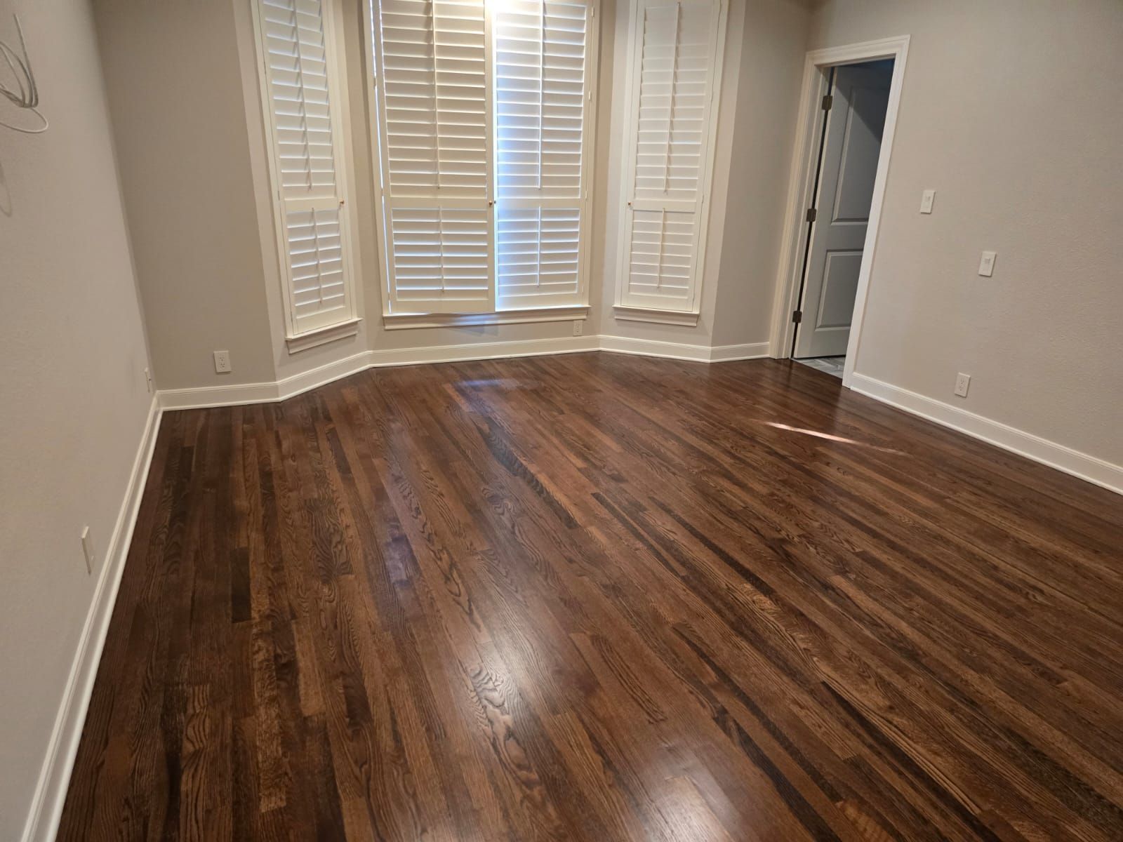 Dark hardwood floors in a room with a bay window with white shutters.