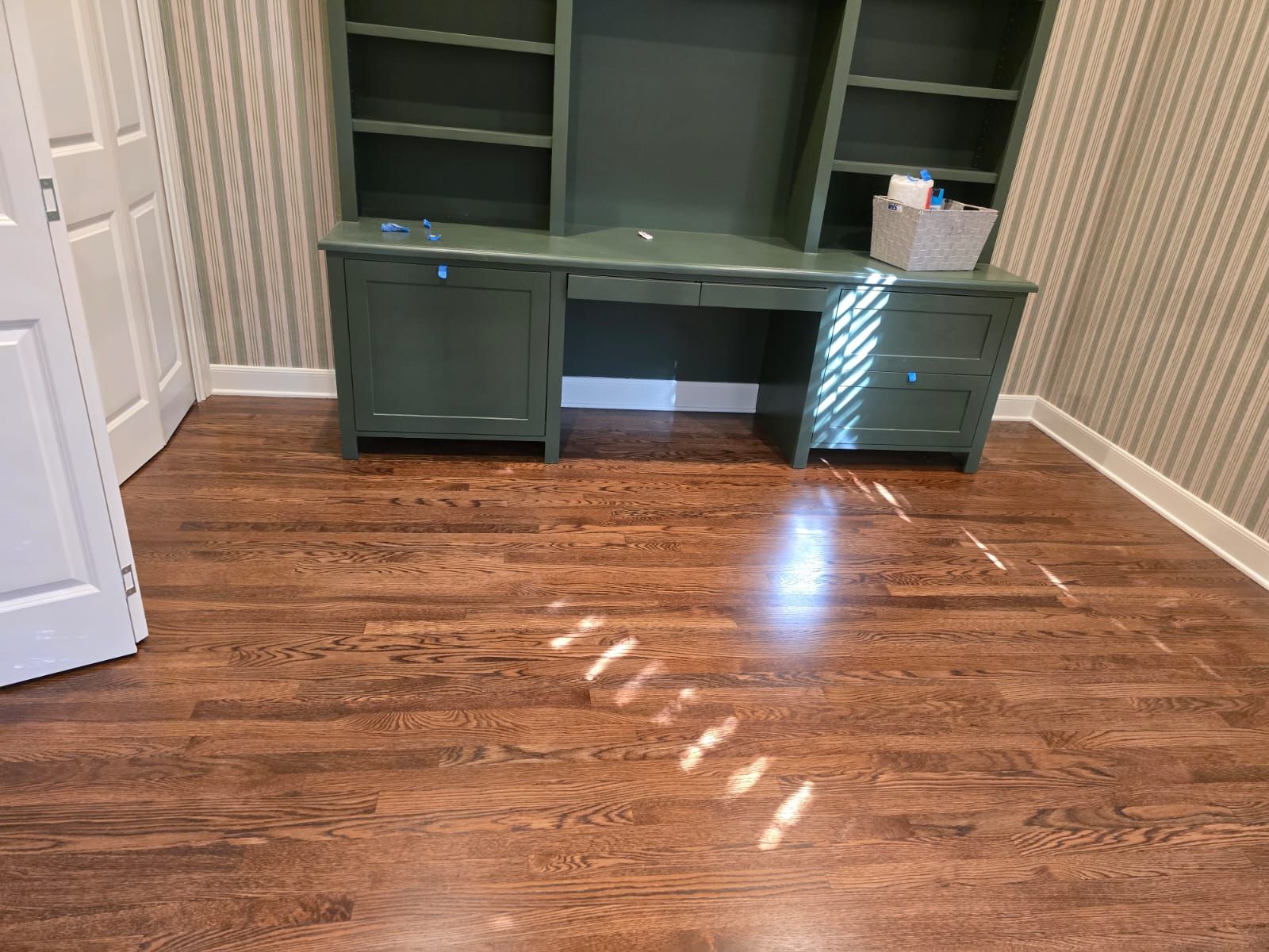 A dark wooden floor in a room with a green desk, shelves, and striped wallpaper.