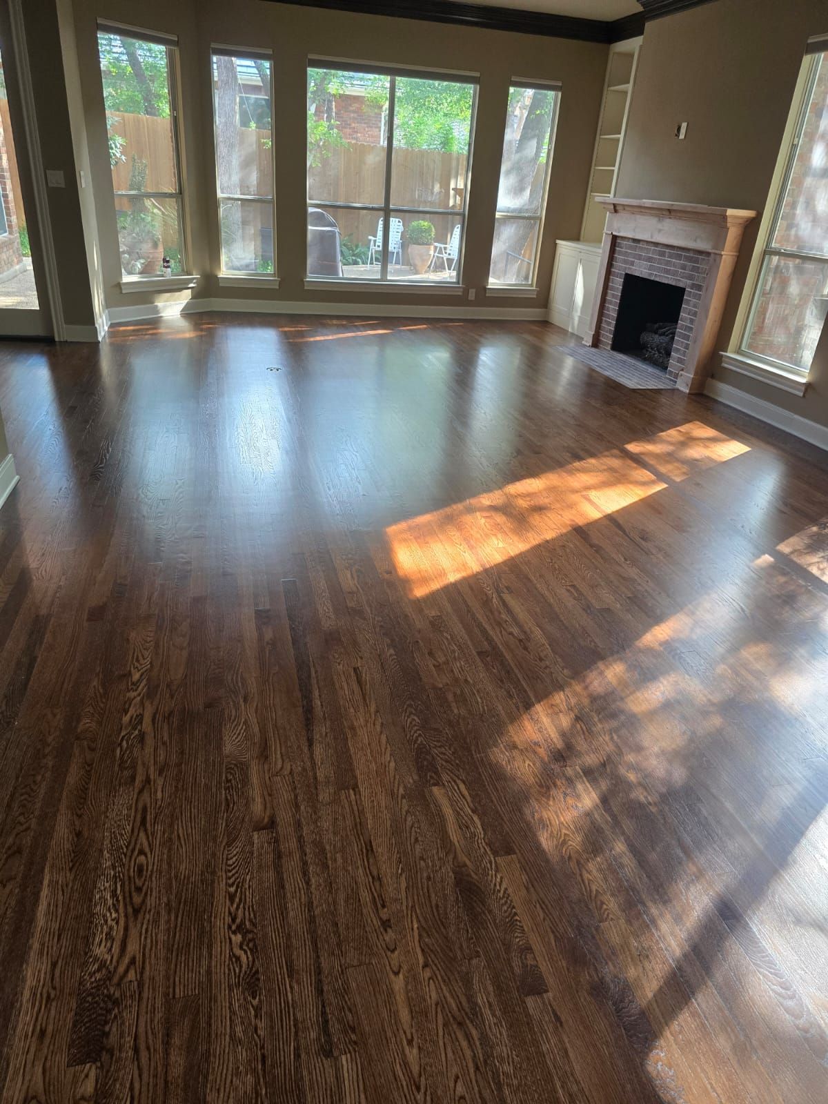 Hardwood floor in a living room, with sunlight across it; a fireplace and windows are also visible.