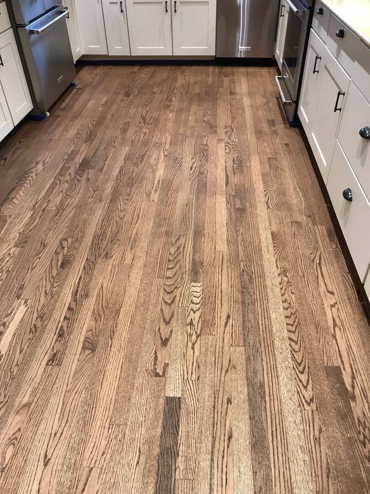 A kitchen with hardwood floors , white cabinets and stainless steel appliances.