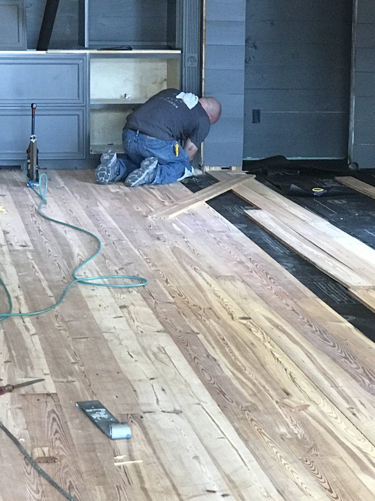 A man is kneeling on a wooden floor in a room.