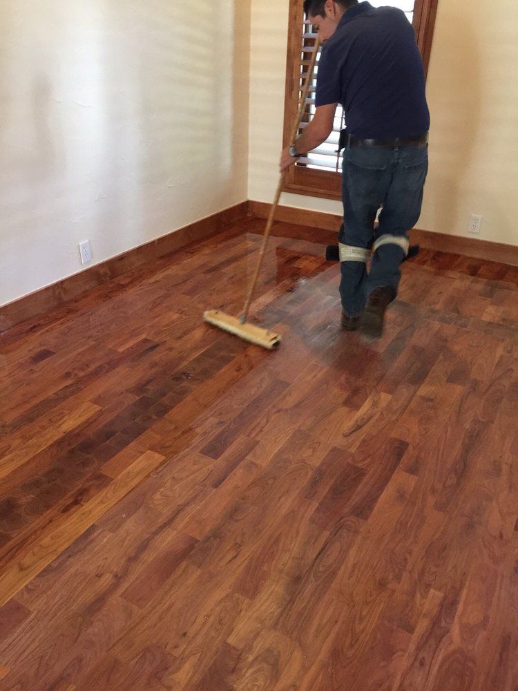 A man is cleaning a wooden floor with a mop.