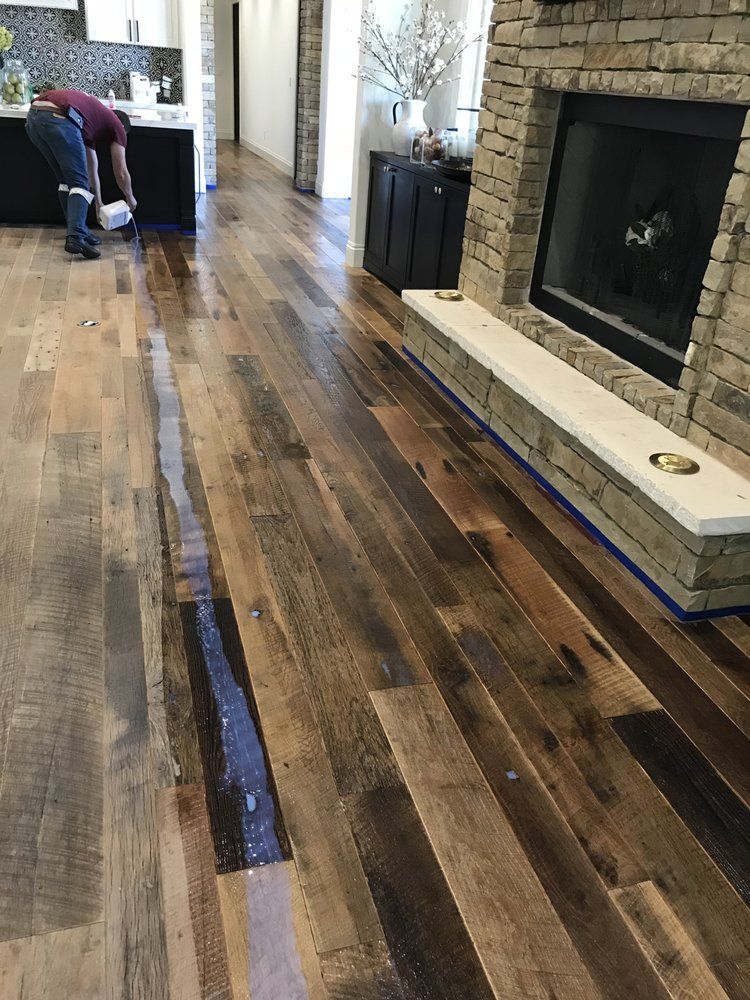 A man is painting a wooden floor in a living room.