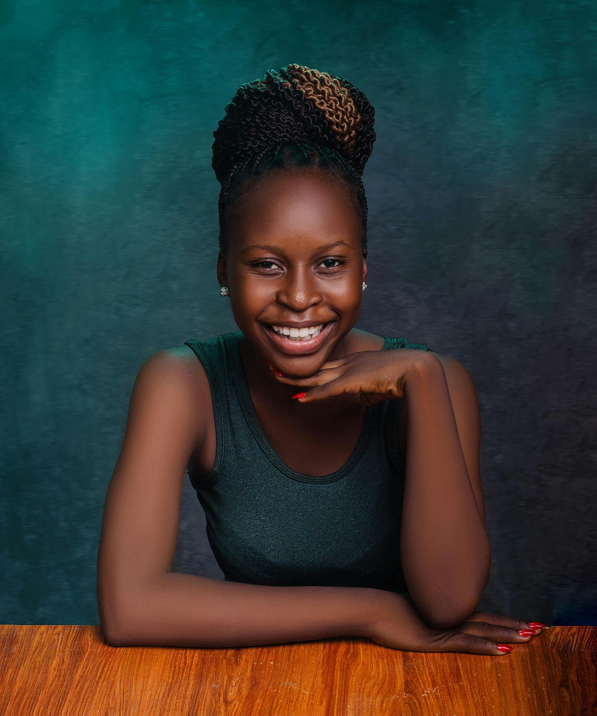 Woman with a bun hairstyle, smiling, leaning on a wooden surface, against a teal and green backdrop.