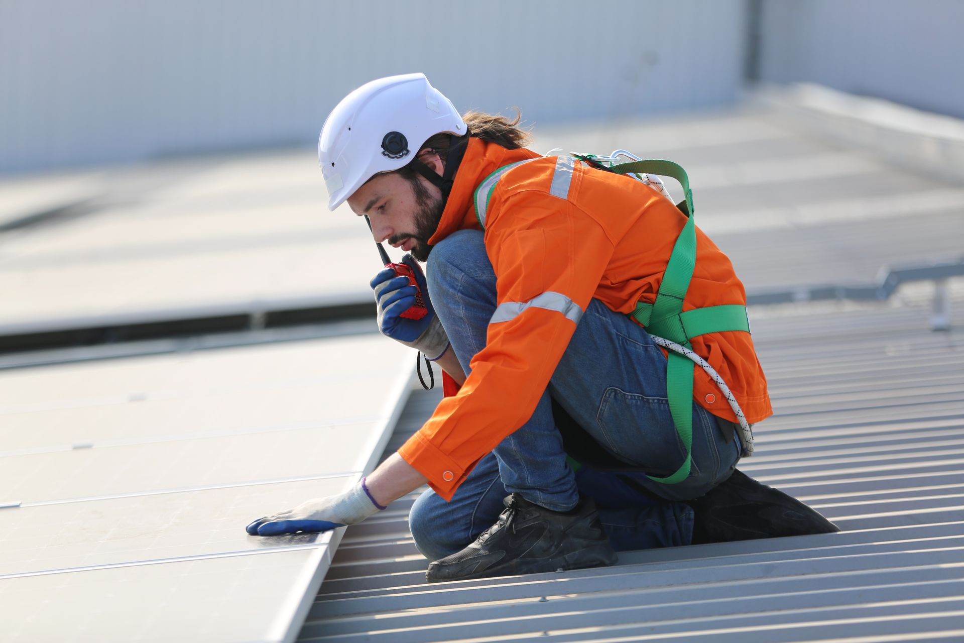 Man in hard hat and vest inspecting a roof, holding a clipboard.