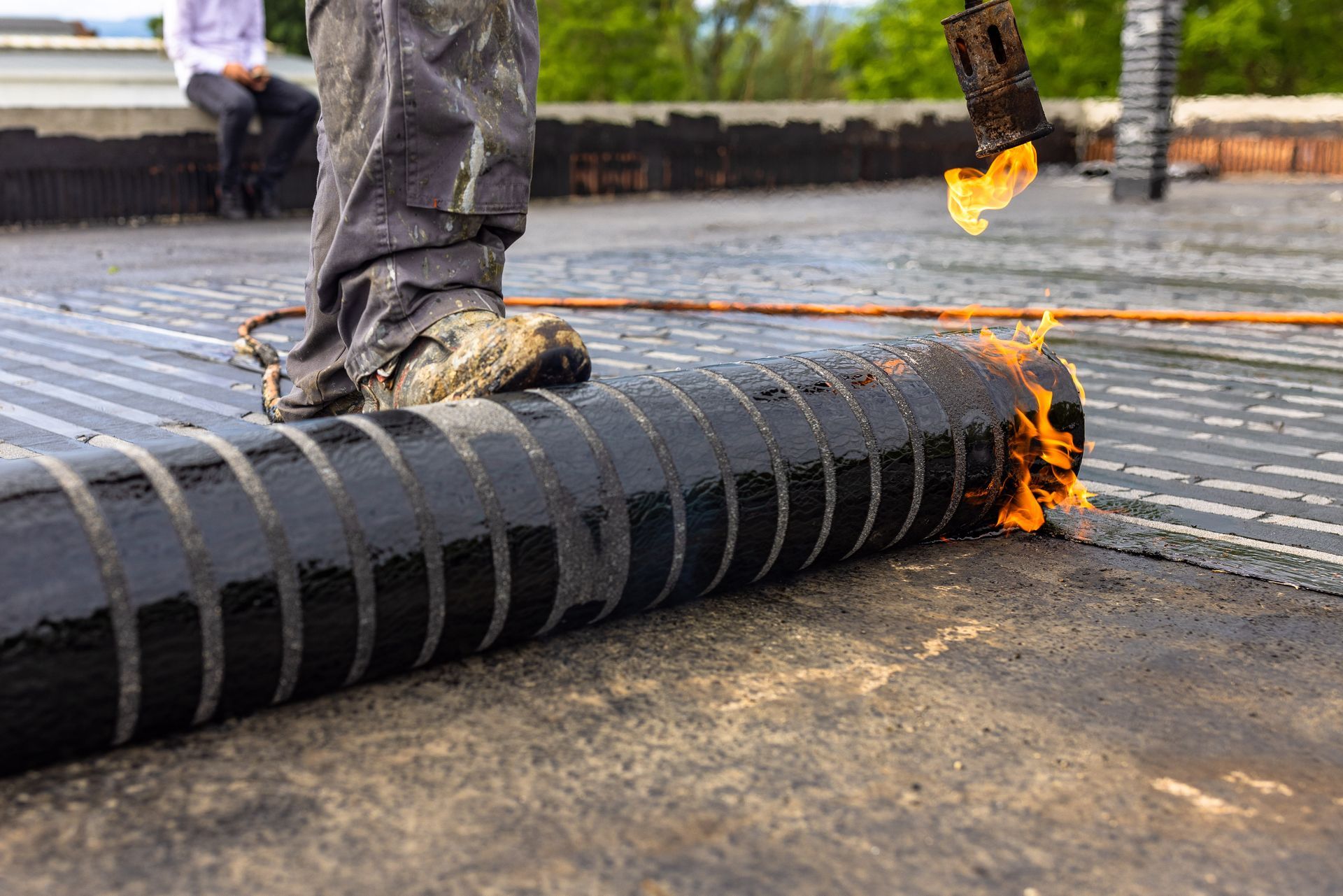 Person kneeling on a roof, using a torch to install roofing material.