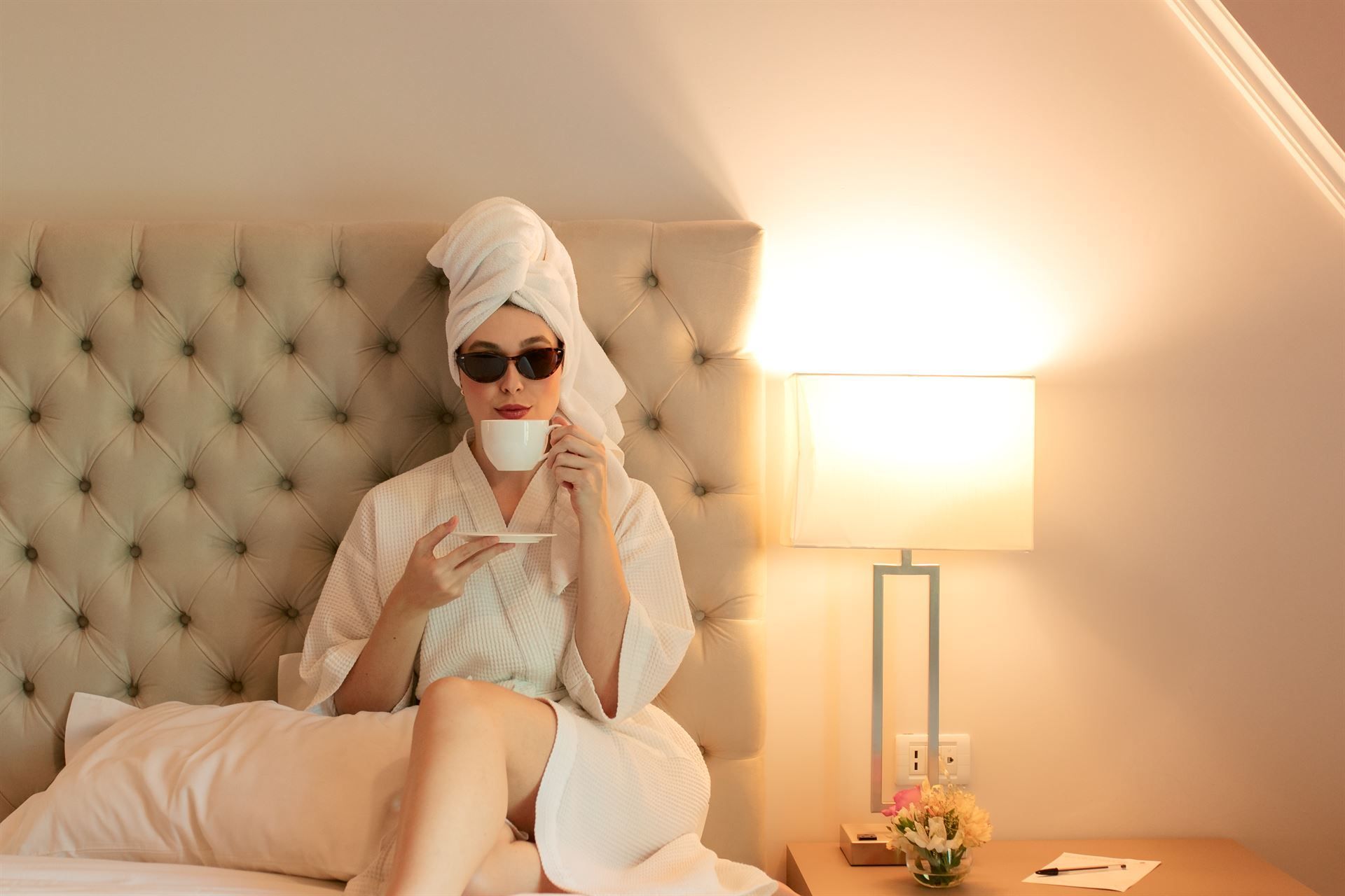 Una mujer en bata de baño está sentada en una cama tomando café.