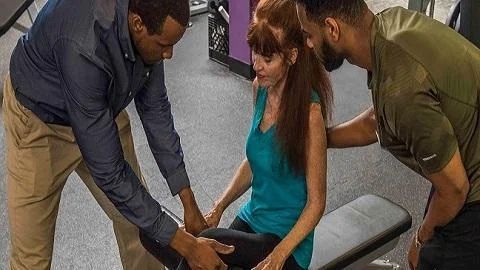 A man is helping a woman sit on a bench in a gym.