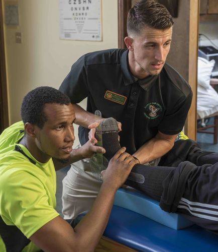 Two men are stretching a person 's leg on a table.