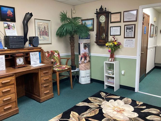 A waiting room with a desk , chair , rug and clock