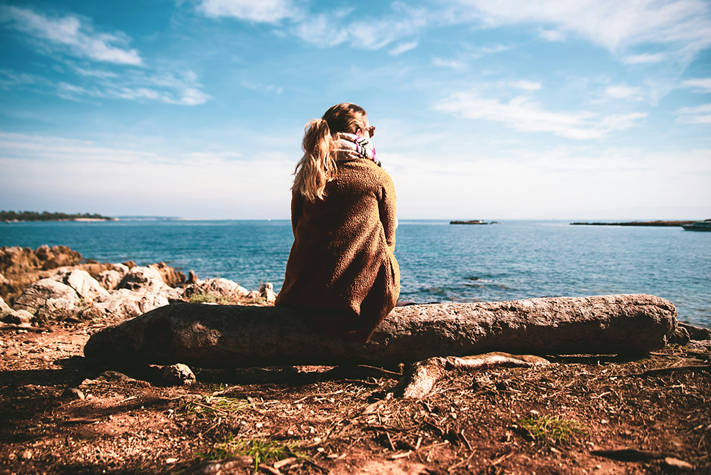 Pensive woman on a log looking out tat the ocean