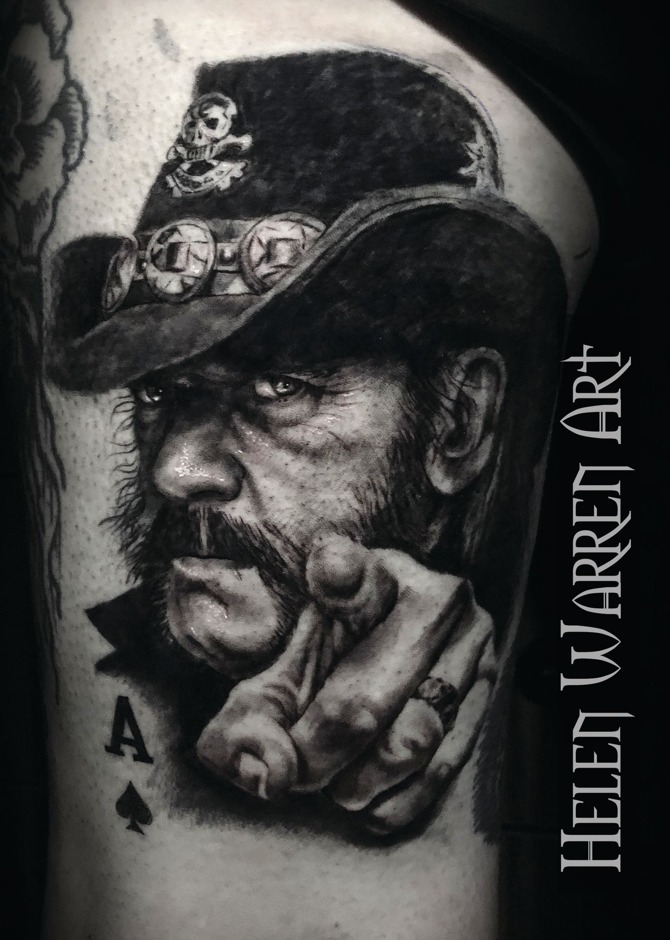Tattoo of Lemmy Kilmister pointing, wearing a hat with a skull and crossbones, ace of spades, black and white.