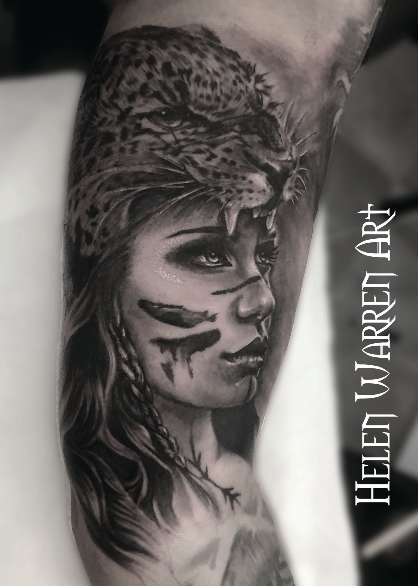 Tattoo of a woman wearing a leopard headdress, face painted, in black and grey, looking to the side.