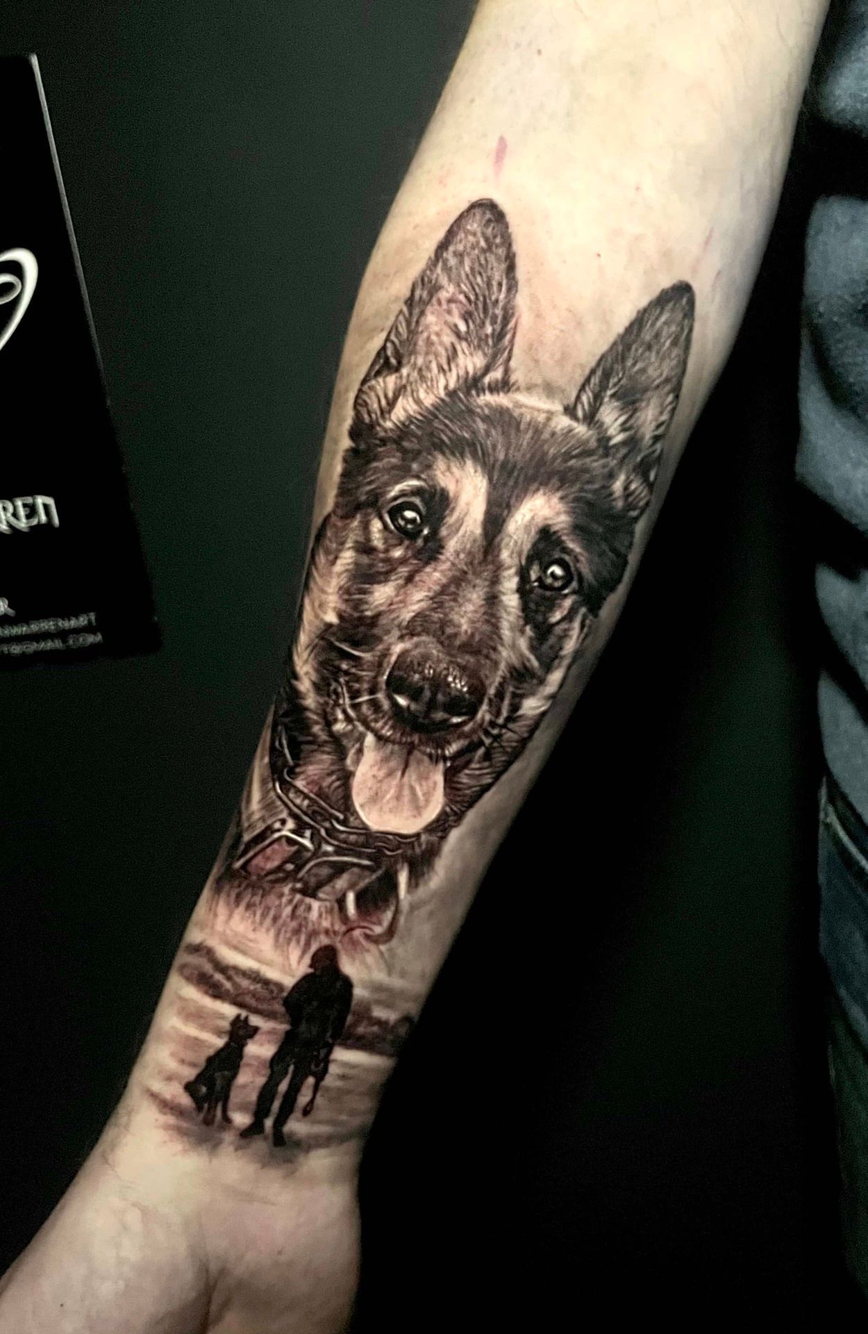 Black and white tattoo of a German Shepherd's face and a person and dog silhouetted on a beach.