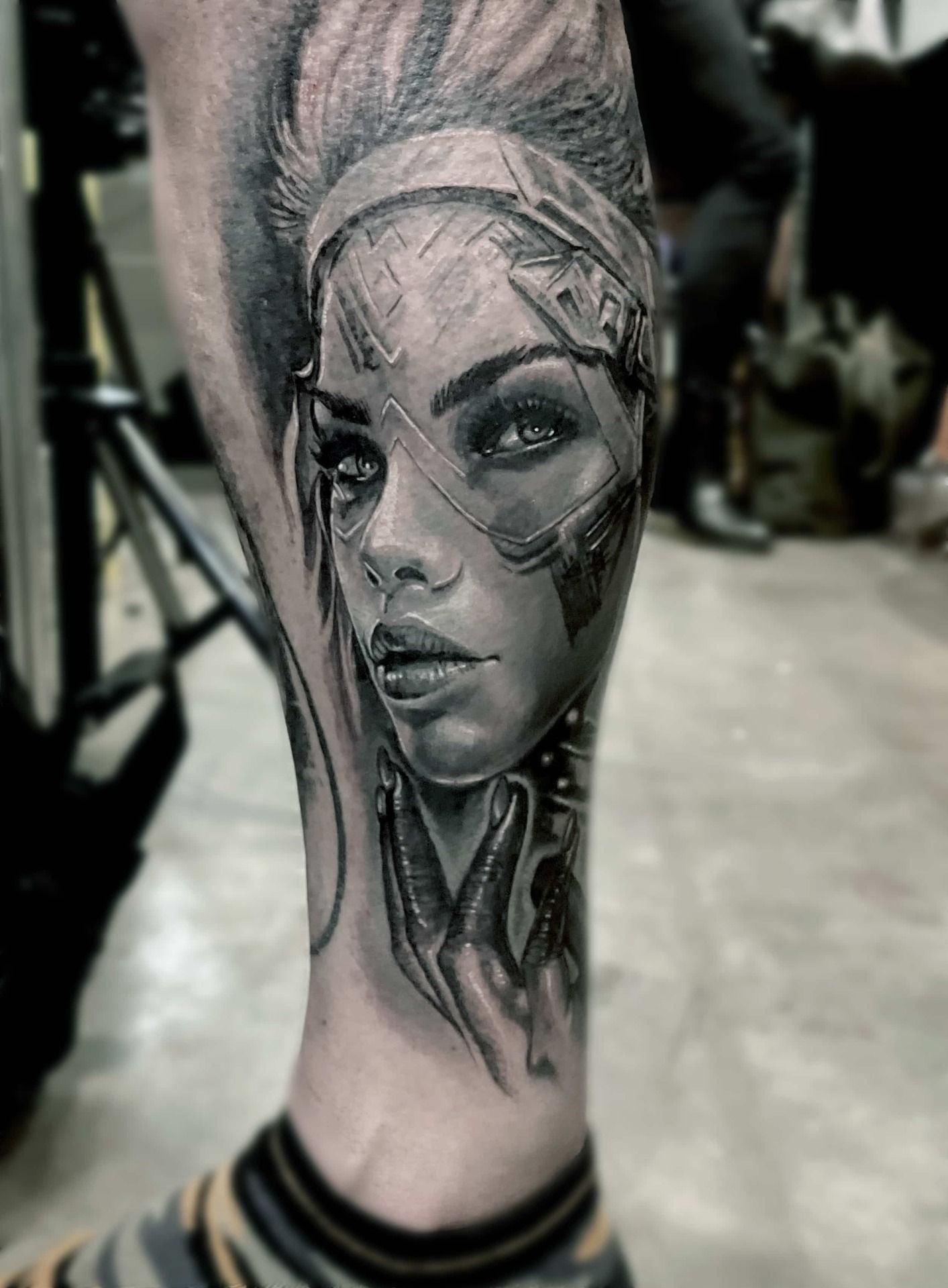 Tattoo of a woman's face with futuristic accents on a leg. Black and gray, detailed shading.