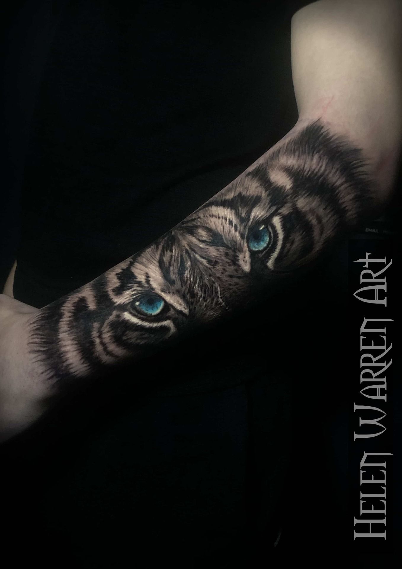 Tiger eye tattoo on an arm, black and gray fur with bright blue eyes.