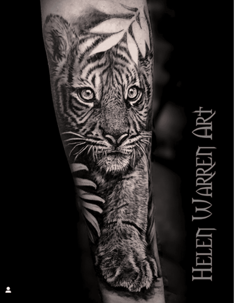 Detailed black and white tattoo of a tiger cub on an arm.