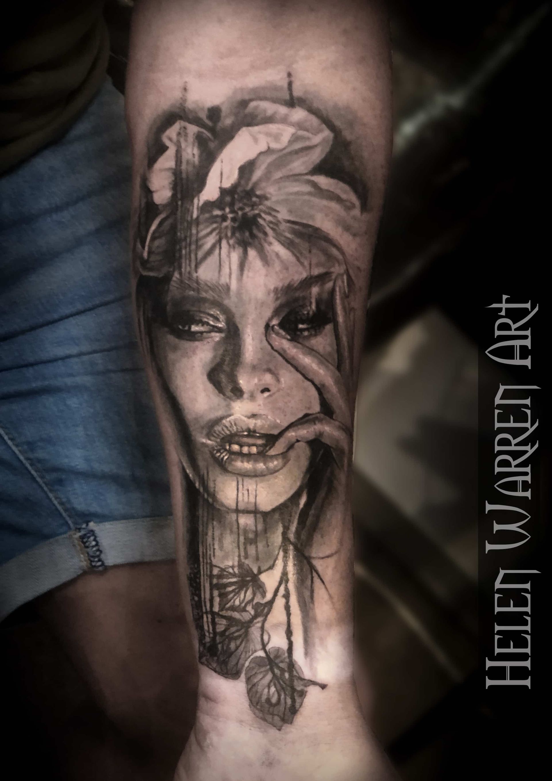 Realistic tattoo on arm of a woman with flower. Black and white, she touches her eye with abstract lines.