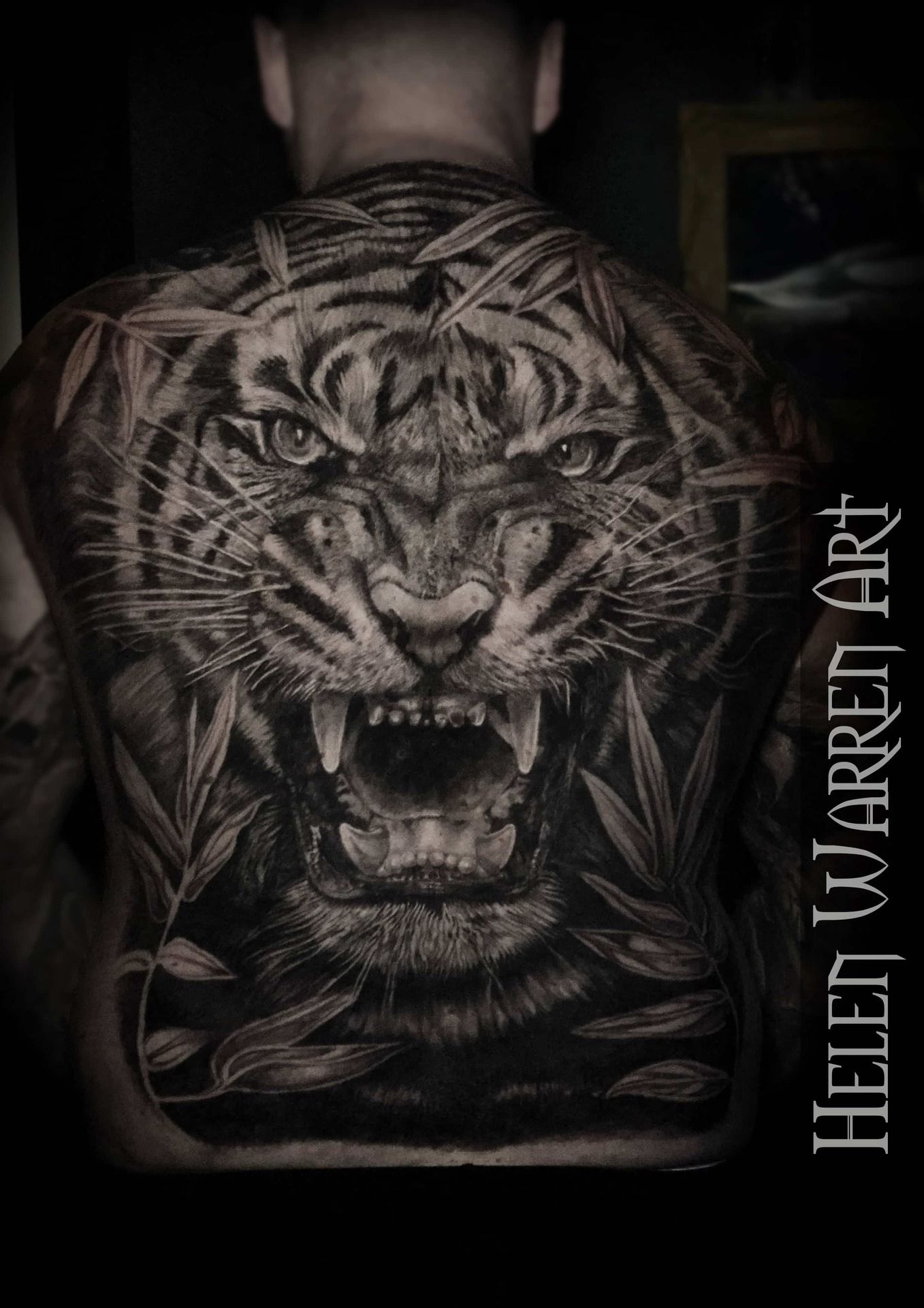 Detailed black and white tiger tattoo roaring on a person's back, framed by bamboo leaves.