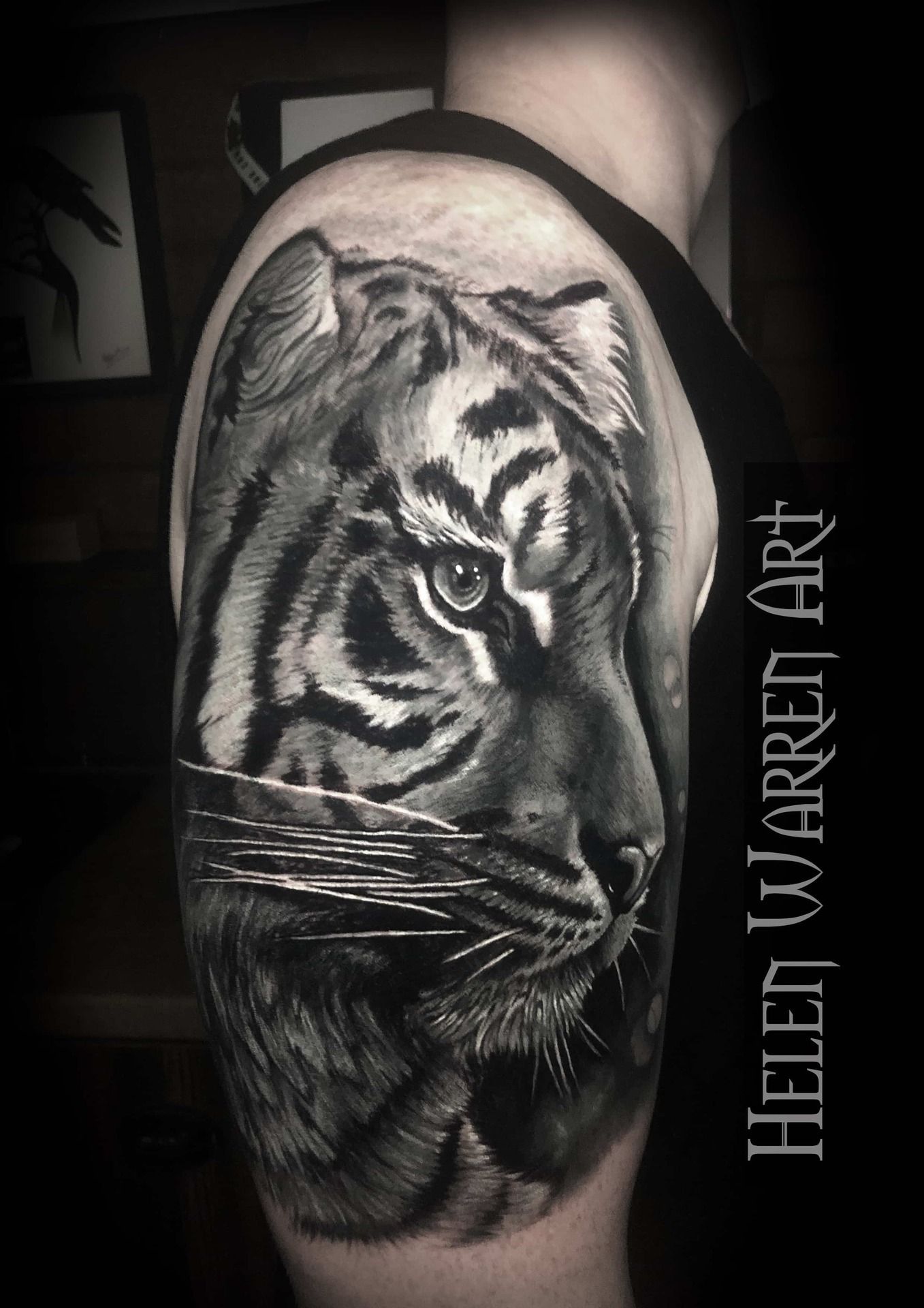 Black and white tattoo of a tiger emerging from water, on a person's upper arm.