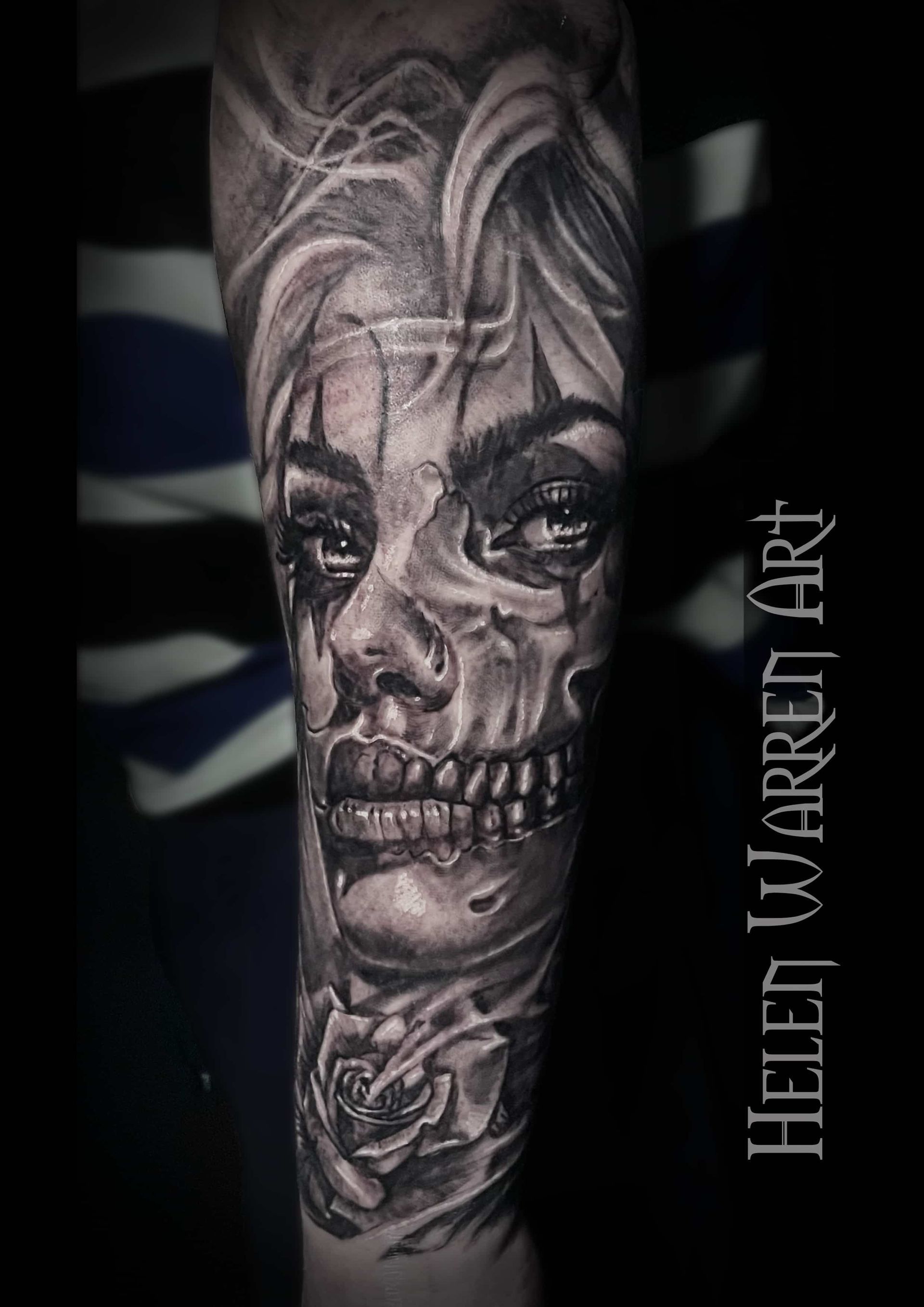 Detailed black and gray tattoo: half-skull, half-woman's face with a rose; on forearm.