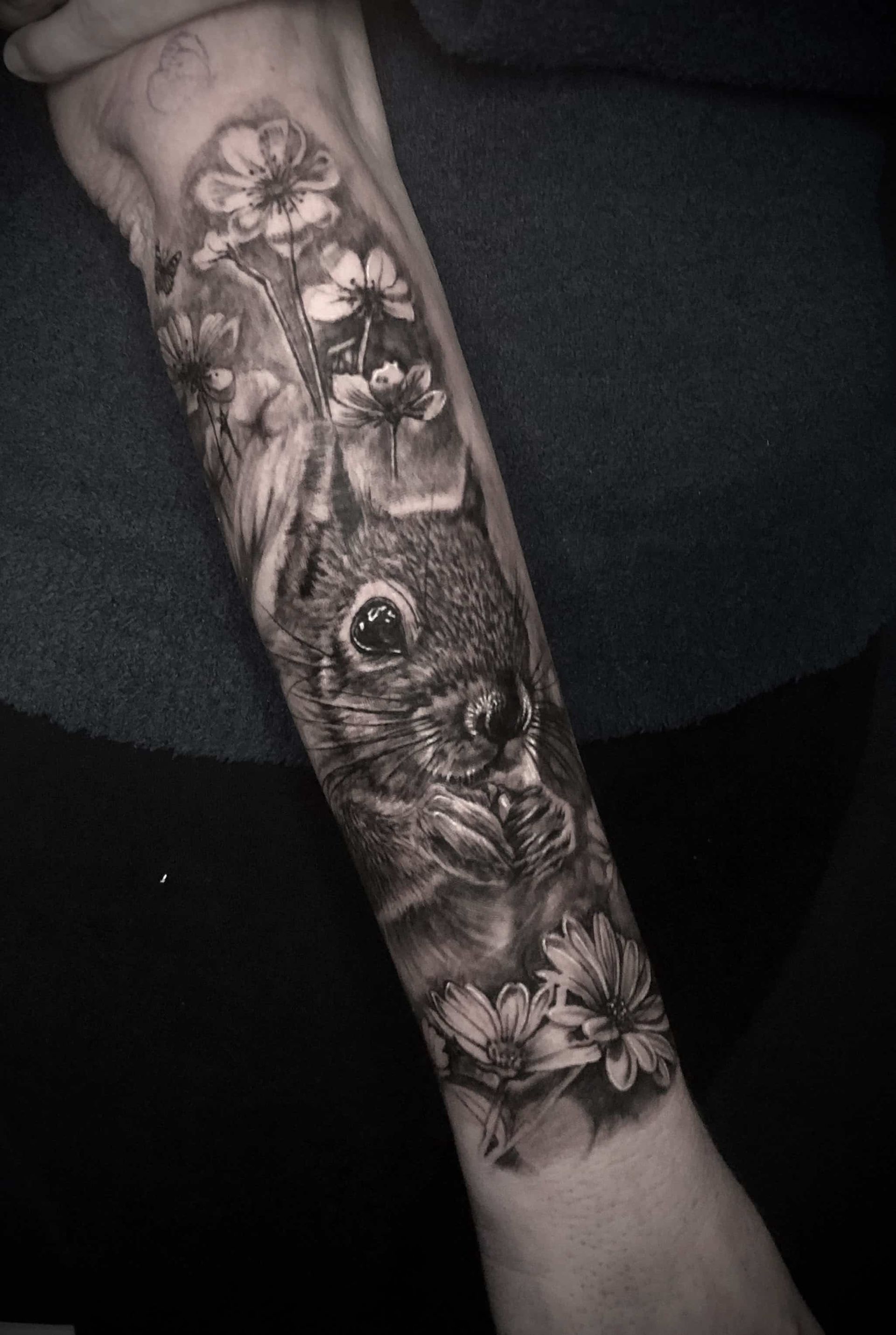 Tattoo of a squirrel among flowers, rendered in grayscale on an arm.
