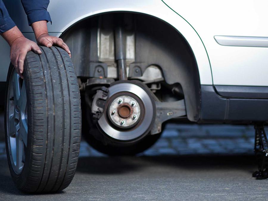 A man is changing a tire on a silver car