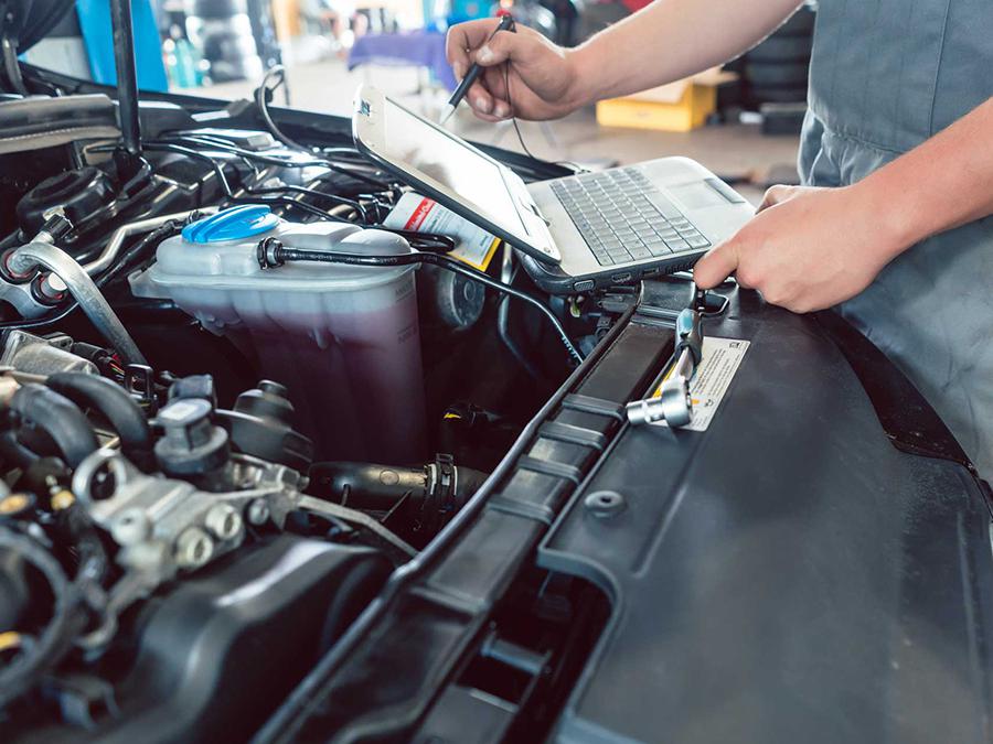 A man is working on a car engine with a laptop.