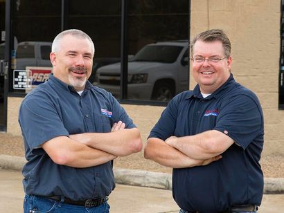 Two men are standing next to each other with their arms crossed in front of a building.