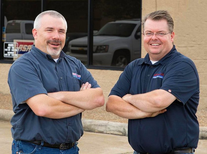 Two men are standing next to each other with their arms crossed in front of a building.