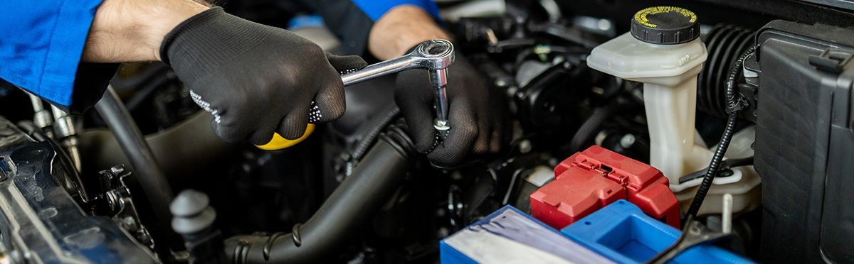 Mechanic working on a car engine, wearing gloves, with a wrench, in a garage setting.