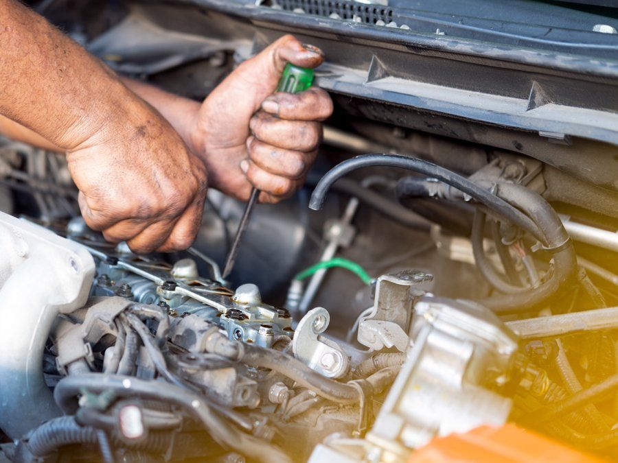 A man is working on a car engine with a screwdriver.