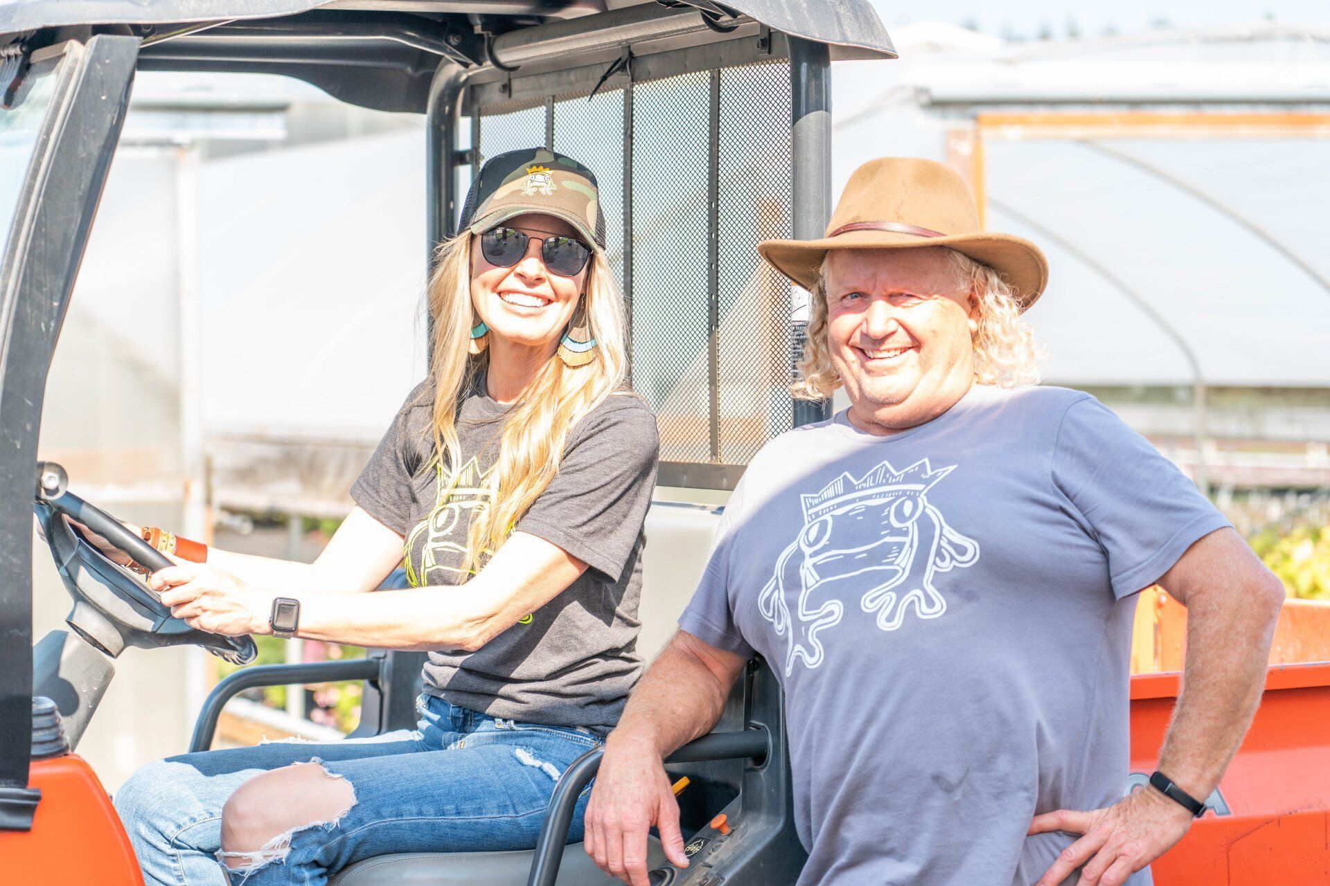 A woman and a man smiling, sitting in a small orange utility vehicle outside.