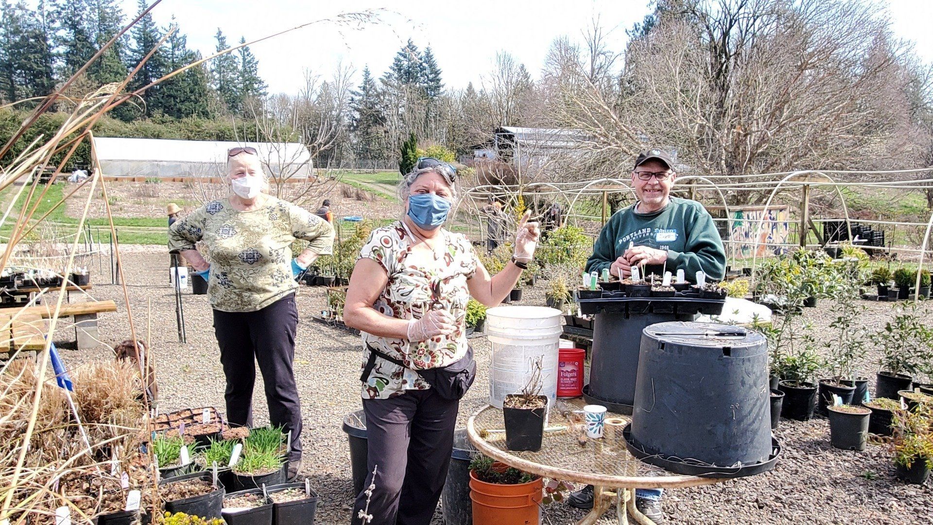 Three people in a garden, one wearing a mask. 
