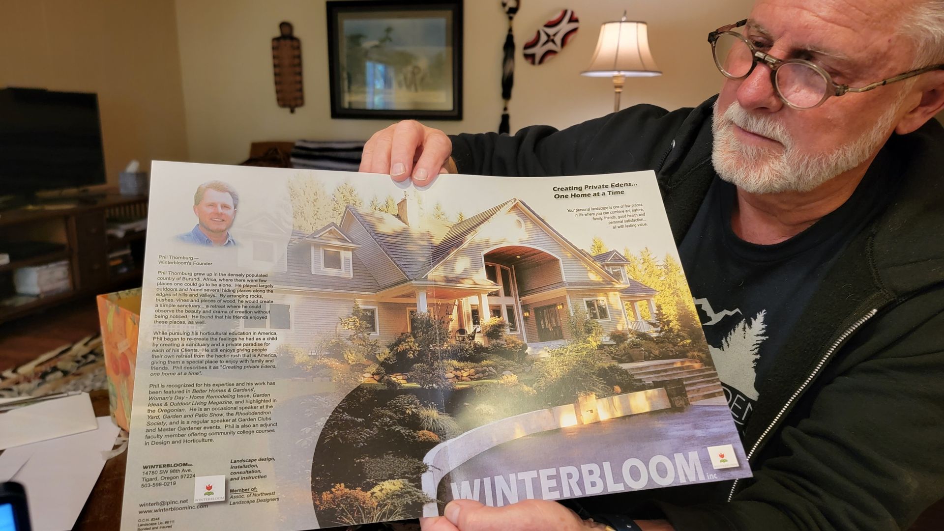Man holding a magazine open to a page with a picture of a house and text. 