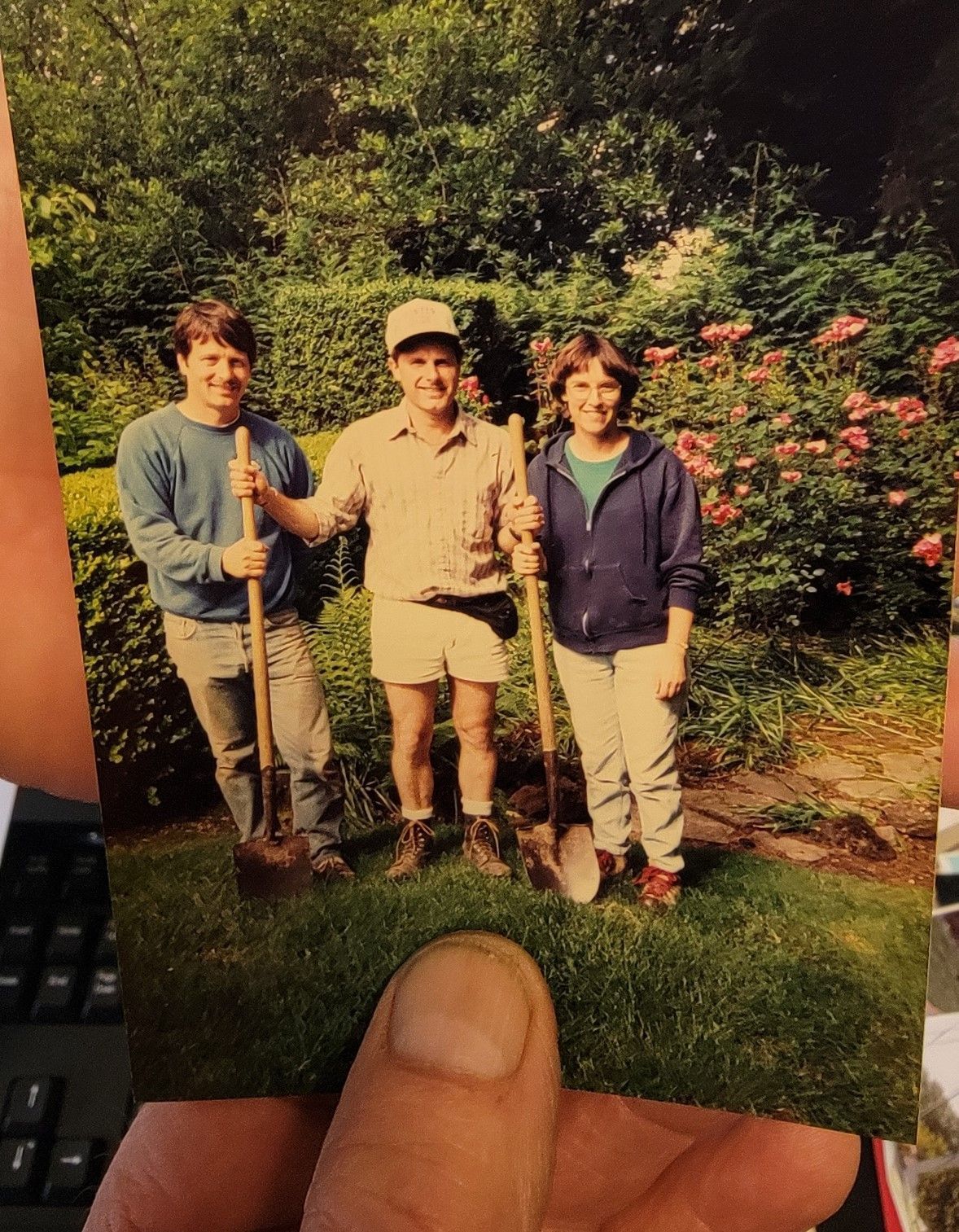 Three people with shovels pose in a garden.