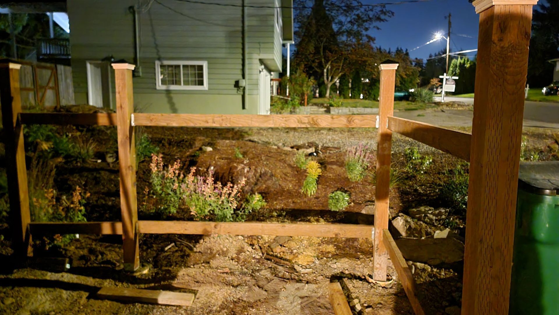 A wooden fence with flowers in a garden bed, under the night sky. 
