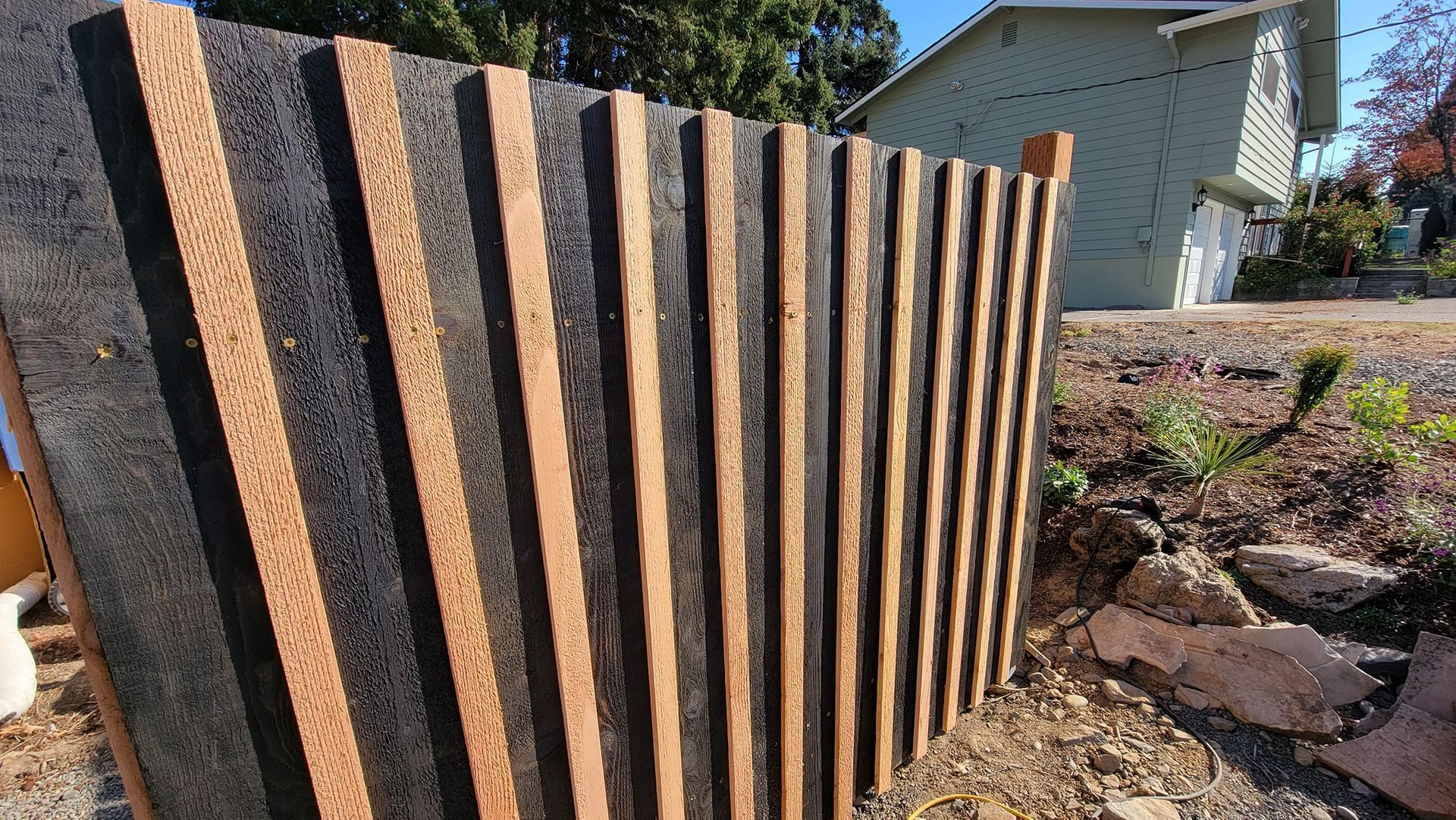 A modern fence design with alternating vertical wooden strips and dark, textured panels.  
