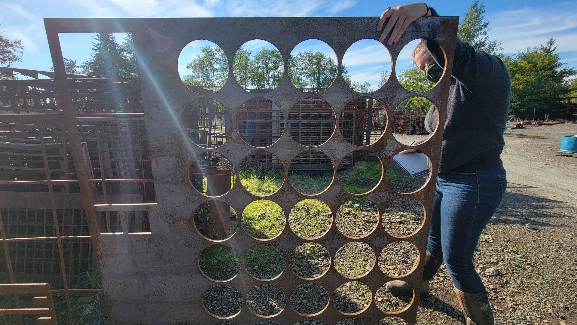 A person installing a large metal sheet with circular cutouts, outdoors on a sunny day.