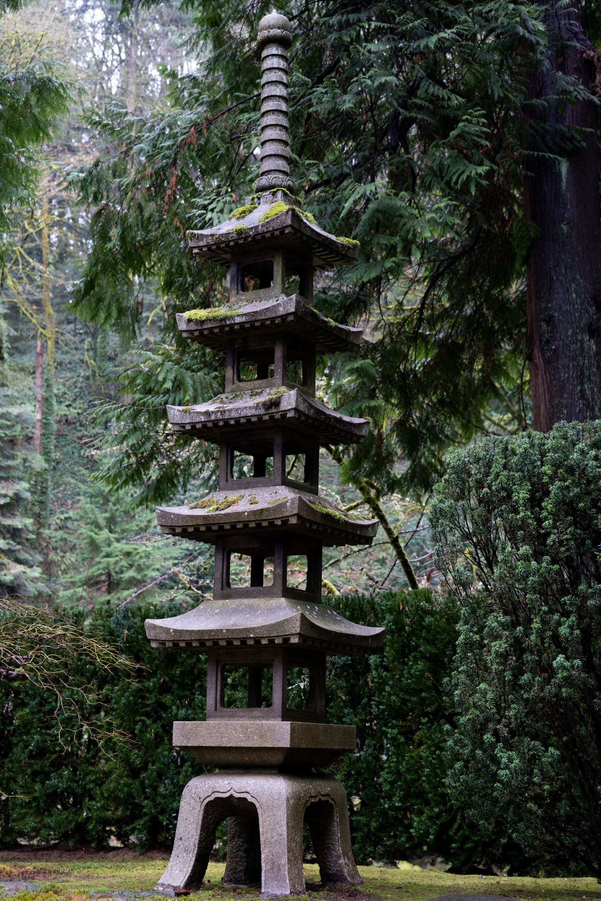 A stone pagoda with multiple tiers stands in a garden surrounded by green foliage.