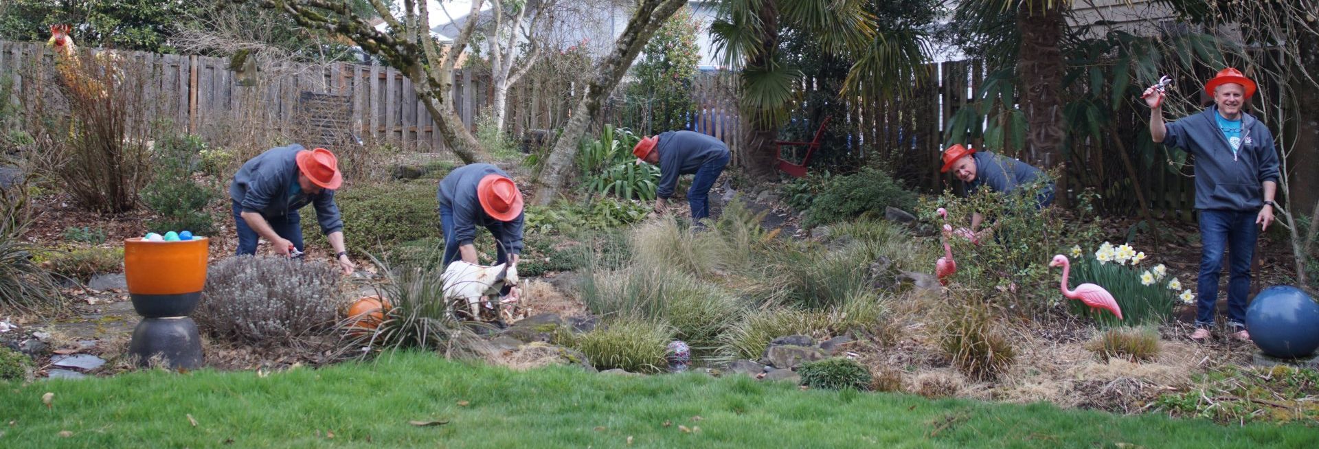 A man in a red hat and dark clothes is tending to a garden. 
