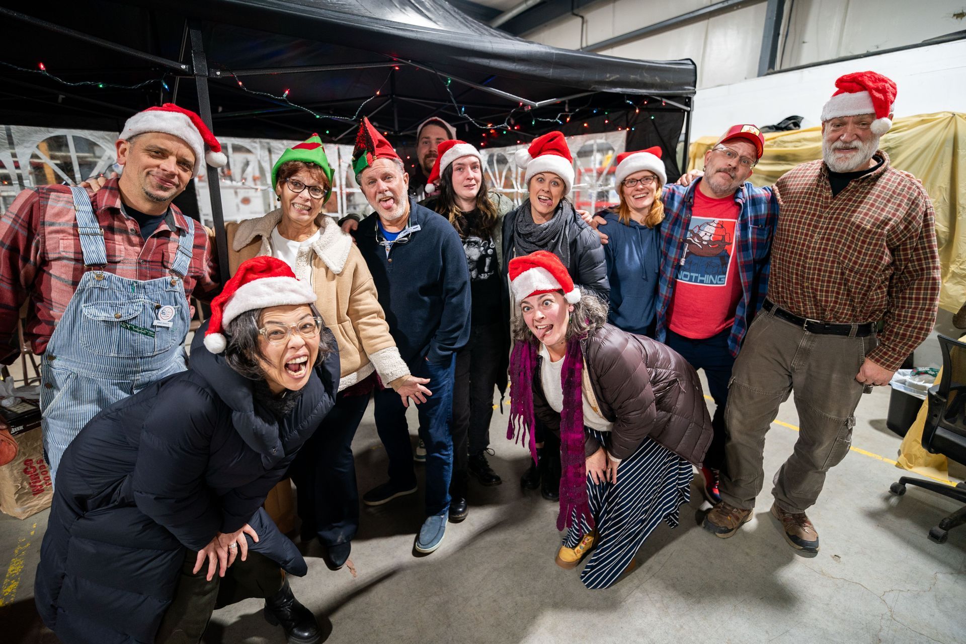 Group of people wearing Santa hats and smiling indoors, likely at a holiday event. 
