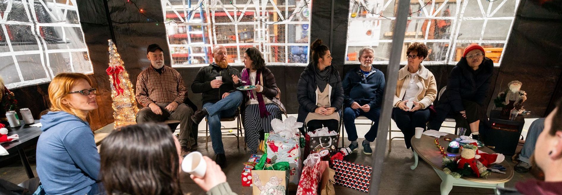 A group of people sit in a room with presents, talking.