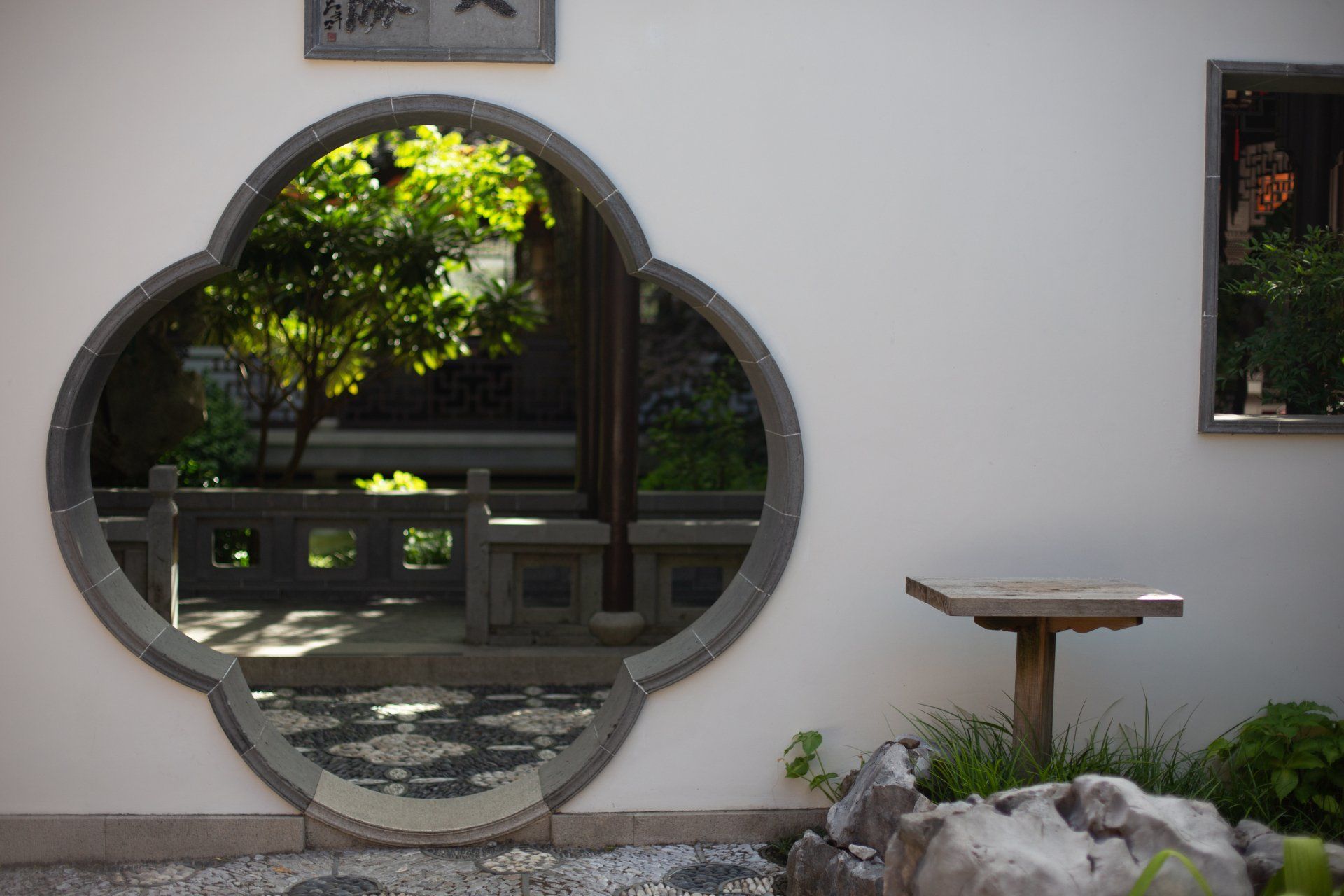 White wall with a quatrefoil-shaped opening framing a view of a garden. 