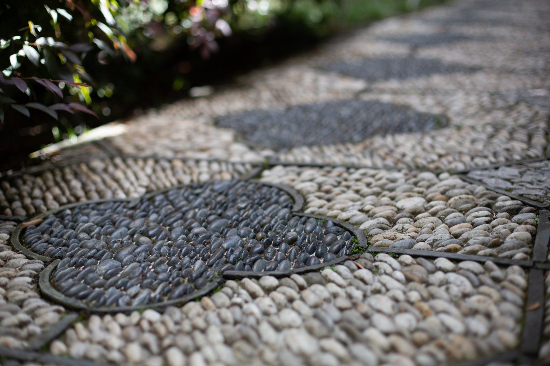 Stone pathway with gray clover-shaped designs, surrounded by white pebbles, leading into the distance.