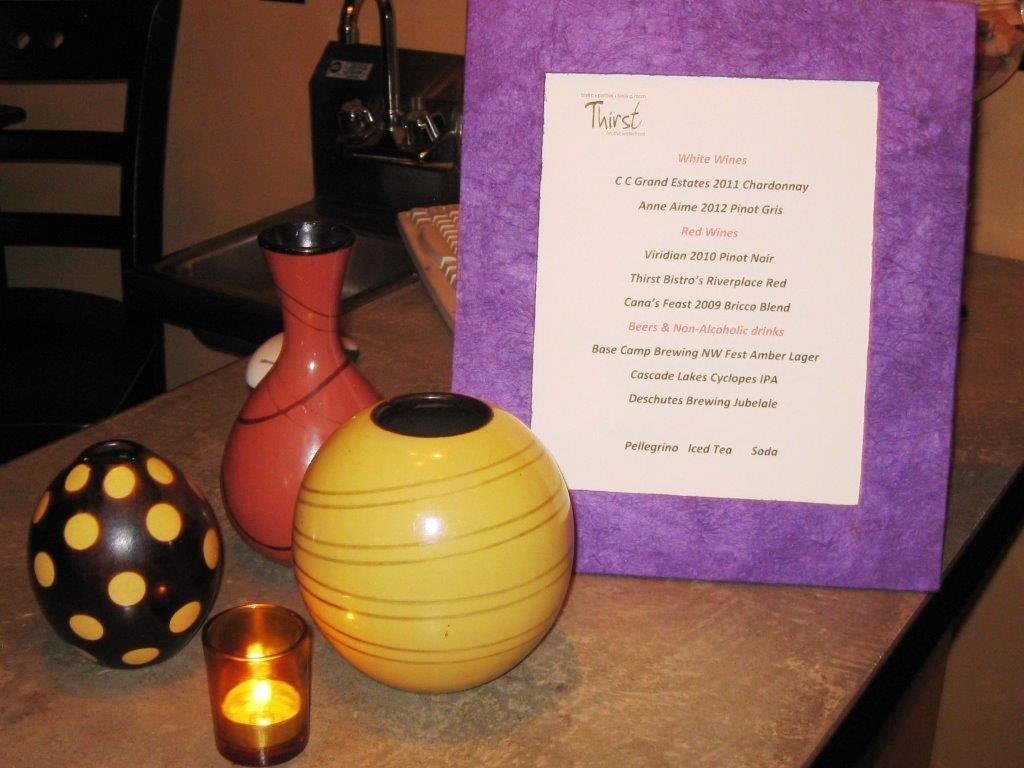 Still life: Purple-framed menu, vases (yellow, pink, black), and lit candle on a countertop.